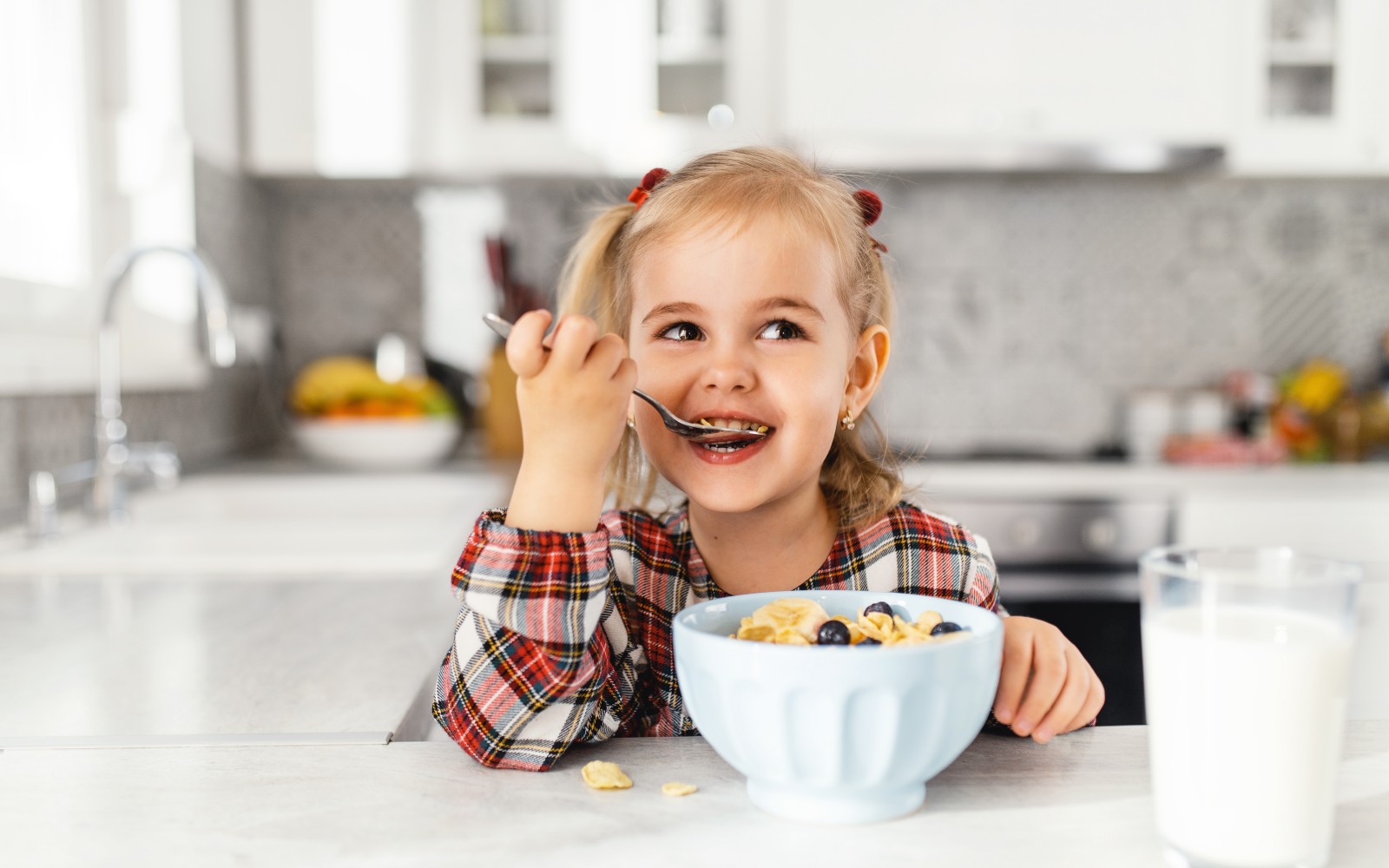 Beautiful little girl having breakfast with cereal, milk and blueberry in kitchen